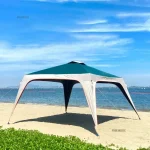 Camping gazebo set up on sandy beach with blue sky and water in background